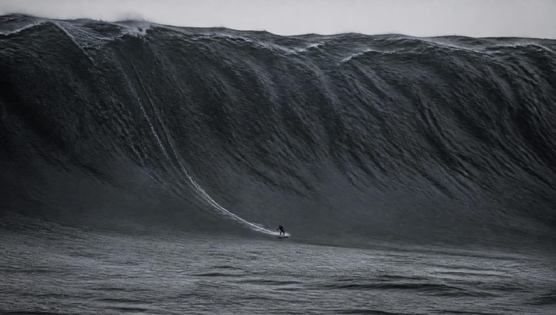 Lone surfer against an enormous wave face